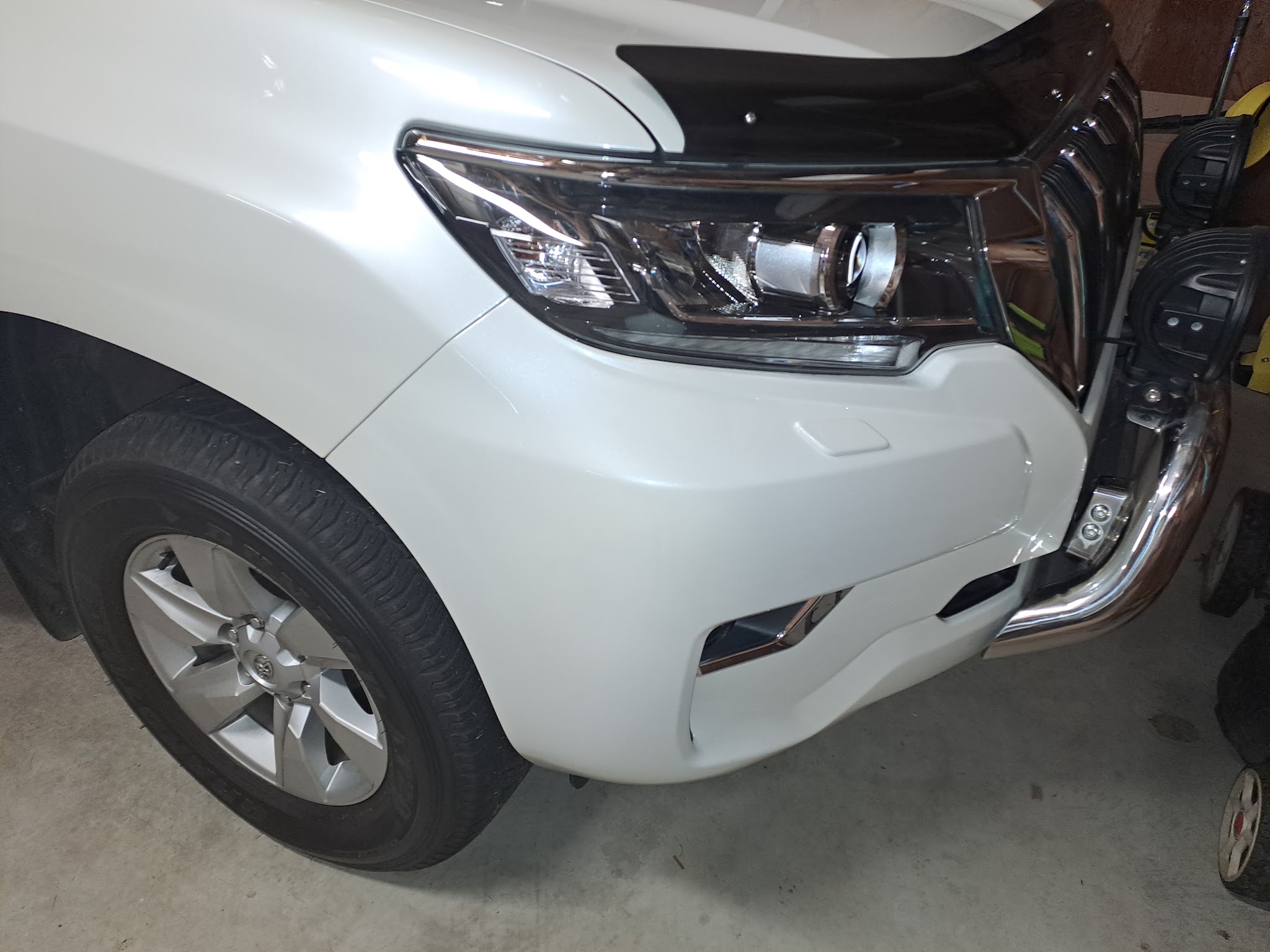 The front guard and headlight of a white Toyota Prado, clean and glossy in the workshop