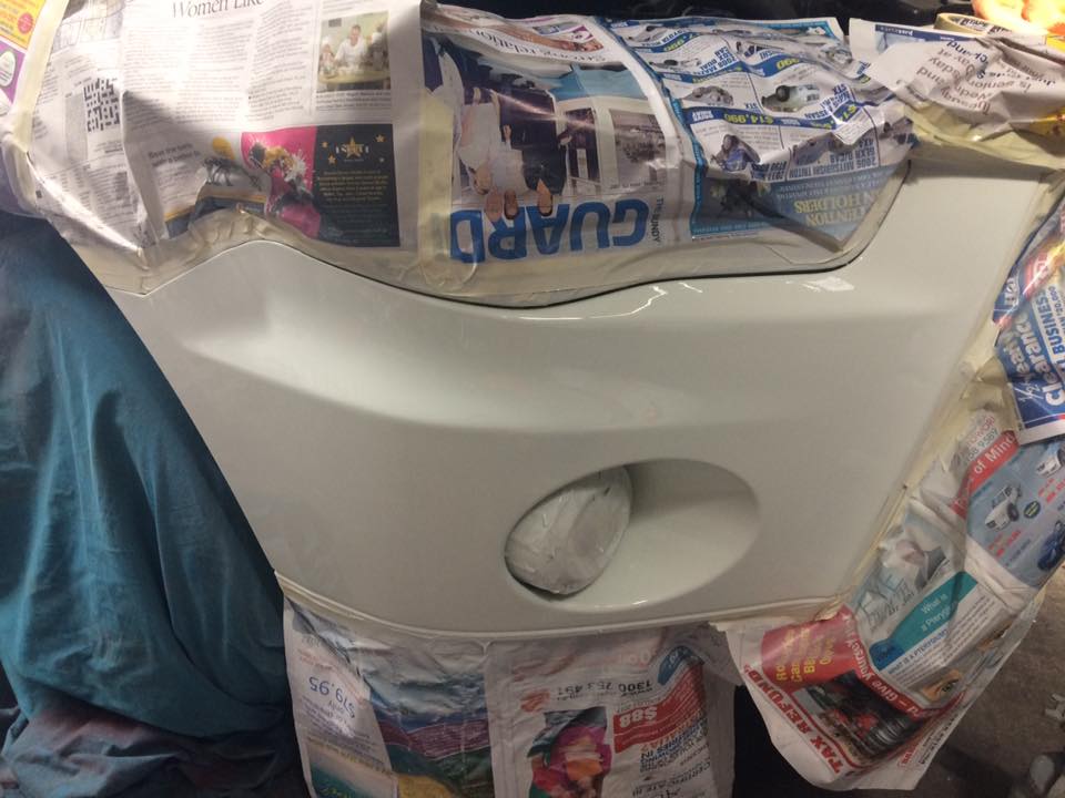 A freshly sprayed white bumper still wrapped in newspaper masking