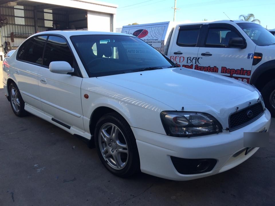 A white Subaru Liberty finished and parked beside the Red Bac ute outside the workshop shed