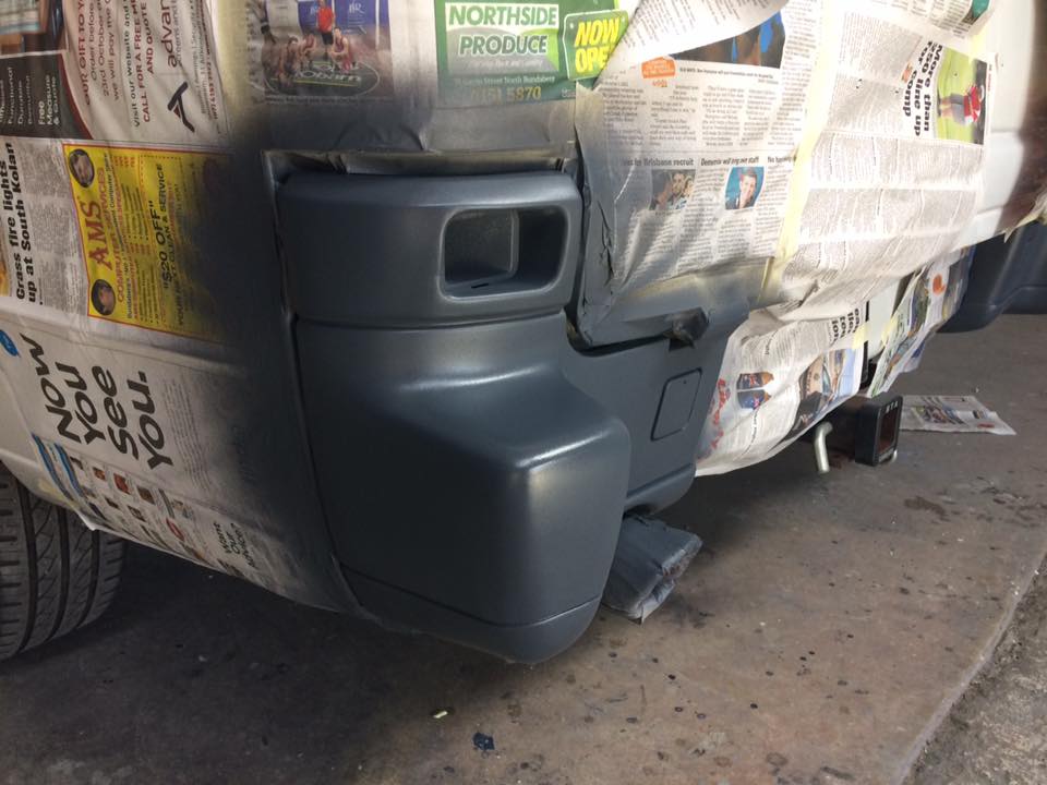 A vehicle bumper fully masked with newspaper and tape, primed and ready for colour