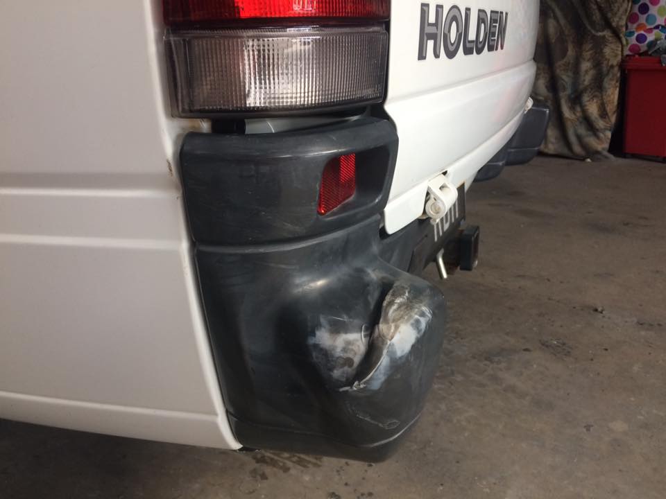 A scuffed and gouged rear bumper corner on a white Holden van in the workshop